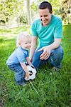 Young Cute Boy and Dad Playing with Soccer Ball in the Park.