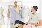 Man sitting with shopping bags while woman selecting a dress in the background