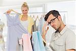 Bored man sitting with shopping bags while woman selecting dress in the background