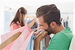 Bored man sitting with shopping bags while woman by clothes rack in the background