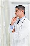 Side view of a thoughtful male doctor with hand on chin standing in the hospital