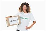 Happy volunteer holding a box of donations with hand on hip on white background