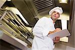 Low angle view of a serious male cook with clipboard standing in the kitchen