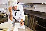 Concentrated male cook writing on clipboard while using cellphone in the kitchen