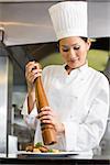 Portrait of a smiling female cook grinding pepper on food in the kitchen