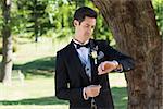 Young attractive groom checking time in garden