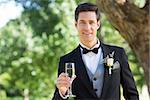 Portrait of handsome groom holding champagne flute in garden