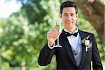 Portrait of smiling groom holding champagne flute in garden