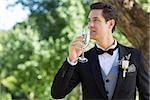Young thoughtful groom drinking champagne in garden