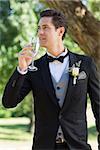 Young thoughtful bridegroom drinking champagne in garden