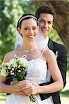 Portrait of groom embracing bride from behind in garden