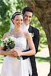 Portrait of happy groom embracing bride from behind in garden