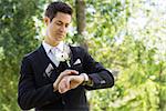 Young smart groom checking time in garden