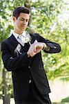 Young smart bridegroom checking time in garden