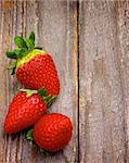 Arrangement of Three Ripe Strawberries with Stems in Corner of Rustic Wooden background