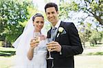 Portrait of newlywed couple toasting champagne in park