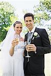 Portrait of bride and groom toasting champagne in park