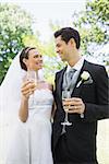 Romantic bride and groom having champagne while looking at each other in park