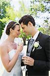 Romantic bride and groom holding champagne flutes in park