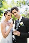 Portrait of beautiful bride and groom holding champagne flutes in park