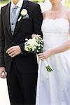 Mid section of young bride and groom holding hands in park