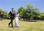 Full length of happy bride and groom holding hands walking in park