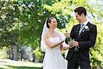 Young newlywed couple opening champagne bottle in park