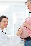 Portrait of beautiful doctor examining pregnant woman with stethoscope in clinic