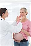 Female doctor examining thyroid glands of pregnant woman in hospital