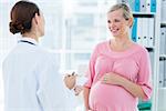 Happy young pregnant woman discussing with female doctor in clinic