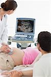 Female doctor performing ultrasound on expectant woman with man sitting by her in clinic