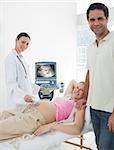 Portrait of smiling expectant couple with doctor performing ultrasound in clinic
