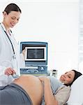 Smiling doctor performing ultrasound on stomach of expectant woman in hospital