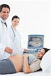 Portrait of confident doctors performing ultrasound on pregnant woman in hospital