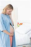 Smiling pregnant woman wearing gown looking at belly in hospital ward