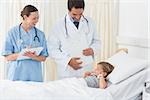 Smiling doctors attending sick girl lying in hospital bed