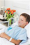 Sick little boy wearing oxygen mask in hospital bed