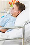 Side view of sick boy wearing oxygen mask in hospital bed