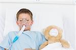 Sick boy wearing oxygen mask sleeping beside stuffed toy in hospital bed