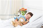 Sick little boy sleeping with teddy bear in hospital bed