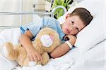 Portrait of sick little boy with teddy bear in hospital bed