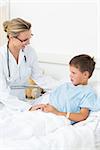 Happy female doctor comforting sick boy in hospital bed