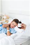 Closeup of doctor holding cough syrup bottle with sick boy in hospital bed