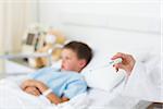 Closeup of doctor holding thermometer with sick boy in hospital bed