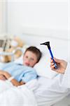 Closeup of doctor holding otoscope with sick boy in hospital bed