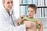 Confident female doctor examining boy with stethoscope in clinic