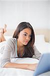 Pretty girl lying on bed using her tablet in her bedroom at home