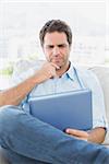 Thinking man sitting on the couch using his tablet at home in the living room