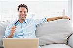 Happy man using laptop sitting on sofa shopping online at home in the living room