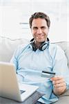 Smiling man sitting on sofa online shopping with laptop at home in the living room